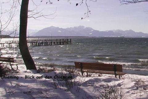 Uitzicht op de Chiemsee vanuit Chieming met besneeuwde oever, banken en bergen op de achtergrond.