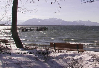 View of Chiemsee from Chieming with snowy shore, benches, mountains in the background in winter.