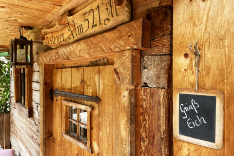 Almhütten-Eingang mit Holzschild 'Alm 521', Laterne und Tafel mit 'Griaß Eich' in Deutschland.