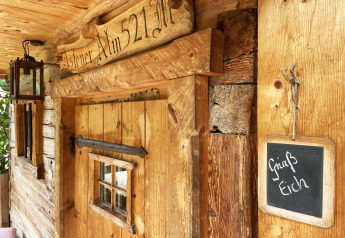 Rustic chalet named 'Alm 521' with a lantern and 'Griaß Eich' sign on wooden wall in Germany.