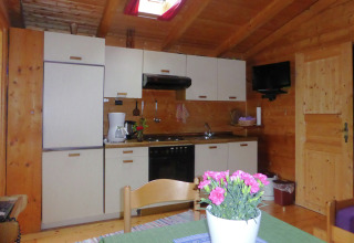 Cozy kitchen inside a chalet in Steingaden, Germany, with wooden walls, appliances, and a dining table.
