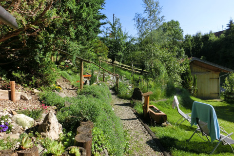 Sunny garden at chalet Steingaden in Germany, with gravel path, green plants, and lounge chairs.