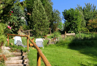A lush green garden with sun loungers and wooden stairs at Chalet Steingaden, Germany, surrounded by trees.