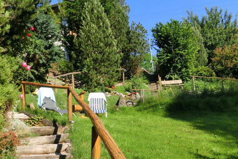 A lush green garden with sun loungers and wooden stairs at Chalet Steingaden, Germany, surrounded by trees.