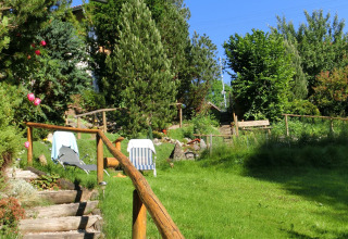 A lush green garden with sun loungers and wooden stairs at Chalet Steingaden, Germany, surrounded by trees.