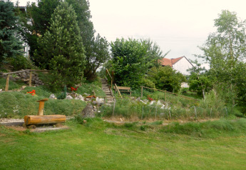 Giardino verde con alberi, fiori, scale e panchina vicino a uno chalet a Steingaden, Germania, in estate.