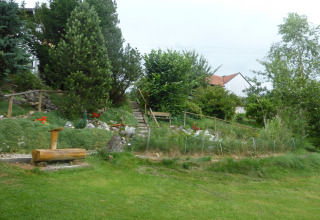 Green garden with trees, flowers, stairs, and bench near a chalet in Steingaden, Germany, in summer.
