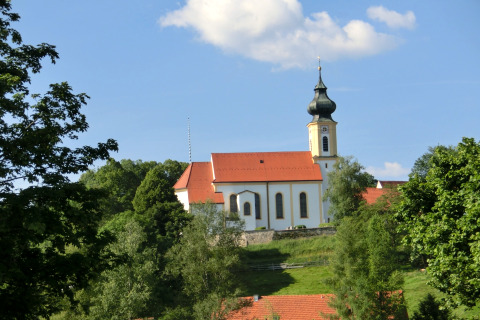 View of the Steingaden chalet in Germany with a traditional church, green trees, and blue sky.