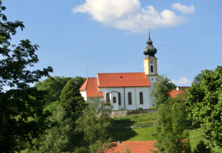 View of the Steingaden chalet in Germany with a traditional church, green trees, and blue sky.
