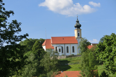 View of the Steingaden chalet in Germany with a traditional church, green trees, and blue sky.