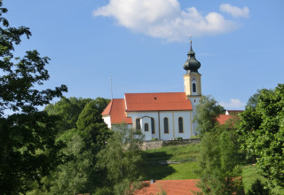 View of the Steingaden chalet in Germany with a traditional church, green trees, and blue sky.