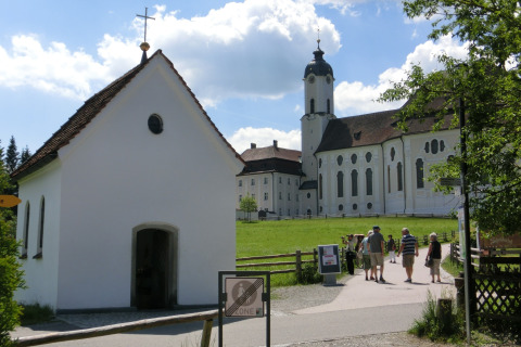Photo of the Steingaden chalet and church in Germany with visitors walking on a sunny day.