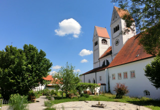 Garden and church with red roofs at Steingaden chalet, blue sky and trees, summer day in Germany.