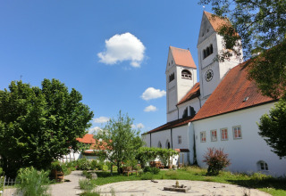 Garden and church with red roofs at Steingaden chalet, blue sky and trees, summer day in Germany.