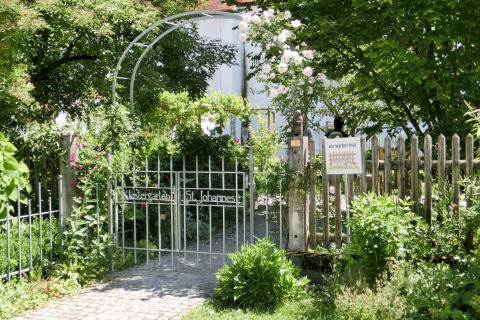 Garden gate with sign, surrounded by greenery and flowers, at the Steingaden chalet in Germany.