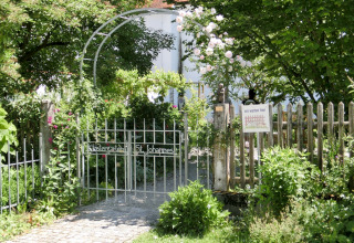 Garden gate with sign, surrounded by greenery and flowers, at the Steingaden chalet in Germany.
