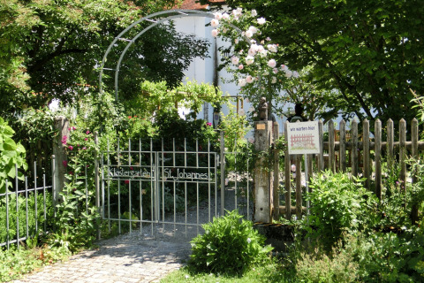 Garden gate with sign, surrounded by greenery and flowers, at the Steingaden chalet in Germany.