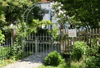 Garden gate with sign, surrounded by greenery and flowers, at the Steingaden chalet in Germany.