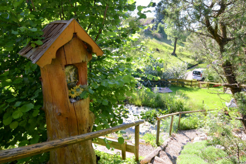 View of a lush garden at Chalet Steingaden in Germany, featuring a wooden figure and greenery.