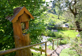 View of a lush garden at Chalet Steingaden in Germany, featuring a wooden figure and greenery.