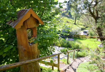 Vista di un giardino rigoglioso allo chalet Steingaden in Germania, con figura di legno e verde.