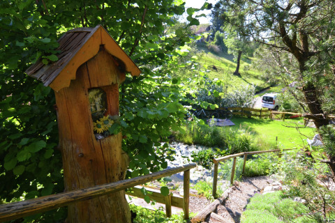 View of a lush garden at Chalet Steingaden in Germany, featuring a wooden figure and greenery.