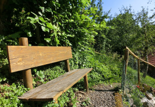 Wooden bench by a gravel path surrounded by lush plants near the Steingaden chalet in Germany.