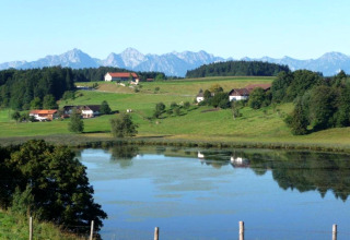 Scenic view from Steingaden chalet in Germany with lake, green fields, forest, and Alps in the distance.