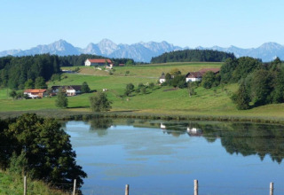 Scenic view from Steingaden chalet in Germany with lake, green fields, forest, and Alps in the distance.