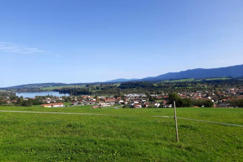 View from the chalet in Steingaden, Germany, showing green fields, a lake, village and distant mountains.
