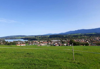 Vista dal chalet di Steingaden, Germania, con prati verdi, lago, paese e montagne in lontananza.