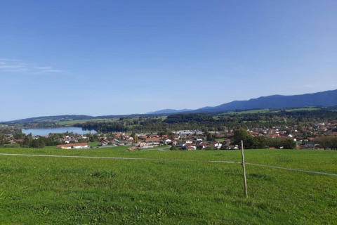 View from the chalet in Steingaden, Germany, showing green fields, a lake, village and distant mountains.