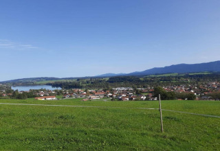 View from the chalet in Steingaden, Germany, showing green fields, a lake, village and distant mountains.