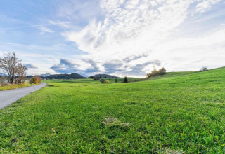 Photo of green fields and a path near the Steingaden chalet in Germany with a dramatic cloudy sky above.