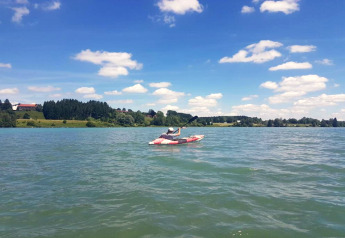 Persona in kayak su un lago vicino allo chalet Steingaden in Germania, con natura e cielo sullo sfondo.