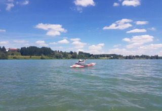 Person kayaking on a lake near Steingaden chalet in Germany, scenic countryside and clouds in view.