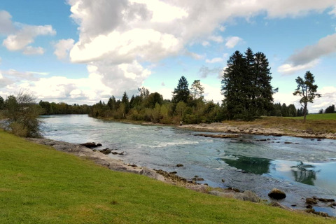 River landscape at Steingaden chalet in Germany with clear water, grassy banks, and trees under a cloudy sky.