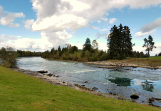 River landscape at Steingaden chalet in Germany with clear water, grassy banks, and trees under a cloudy sky.
