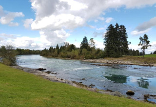 River landscape at Steingaden chalet in Germany with clear water, grassy banks, and trees under a cloudy sky.