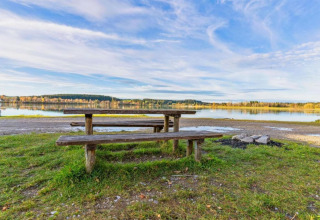 Picnic table and benches by a lake near Steingaden chalet in Germany, with peaceful nature and blue sky.