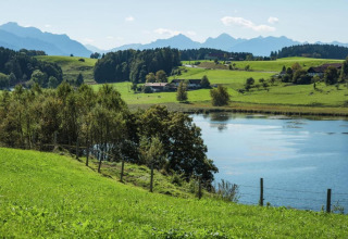 Tranquil landscape at Steingaden chalet in Germany, showing a lake, green fields, trees and distant hills.
