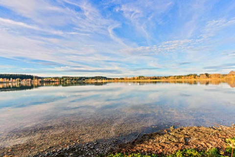 Tranquil lake view with clear water and blue sky, seen from Chalet Steingaden in Germany.