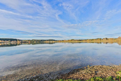 Tranquil lake view with clear water and blue sky, seen from Chalet Steingaden in Germany.