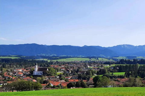 View of Steingaden chalet in Germany, featuring green fields, a church, houses, and distant mountains.