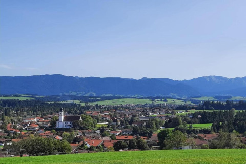 View of Steingaden chalet in Germany, featuring green fields, a church, houses, and distant mountains.