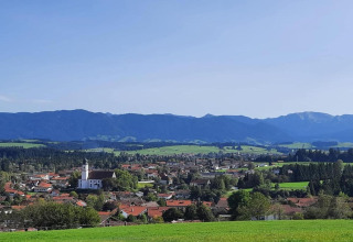 View of Steingaden chalet in Germany, featuring green fields, a church, houses, and distant mountains.
