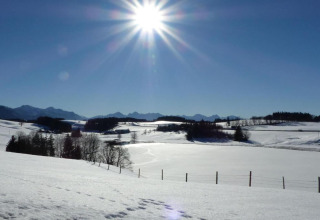 Sunny winter day with snow-covered fields and distant mountains at chalet Steingaden in Germany, blue sky.