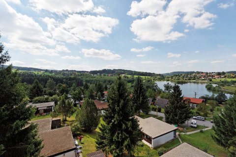 Udsigt over Holiday park «Jägerwiesen 1» i Tyskland med hytter, skov, sø og blå himmel med skyer.