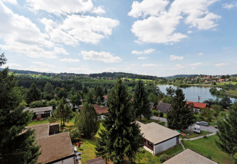 View of Holiday park «Jägerwiesen 1» in Germany with cabins, trees, a lake, and a partly cloudy sky.