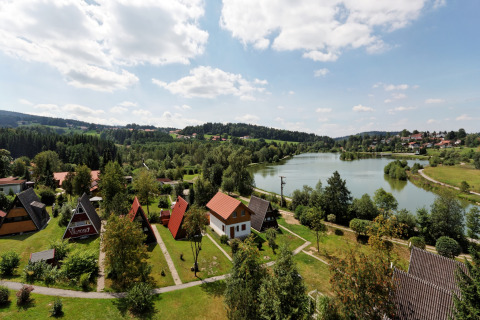 Feriepark Jägerwiesen 1 i Tyskland med sø, grønne områder og charmerende hytter under blå himmel.